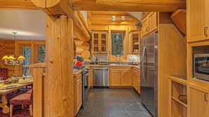 A wooden cabin interior with a kitchen featuring a stainless steel refrigerator, wooden cabinets, and a stone-tiled floor.