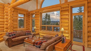 A log cabin interior with a cozy seating area, large windows, and a view of the surrounding forest.