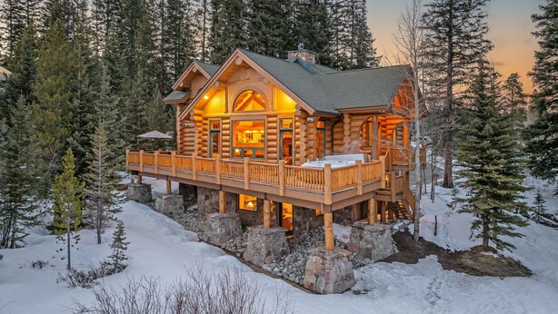 A log cabin with a deck, surrounded by snow and trees.
