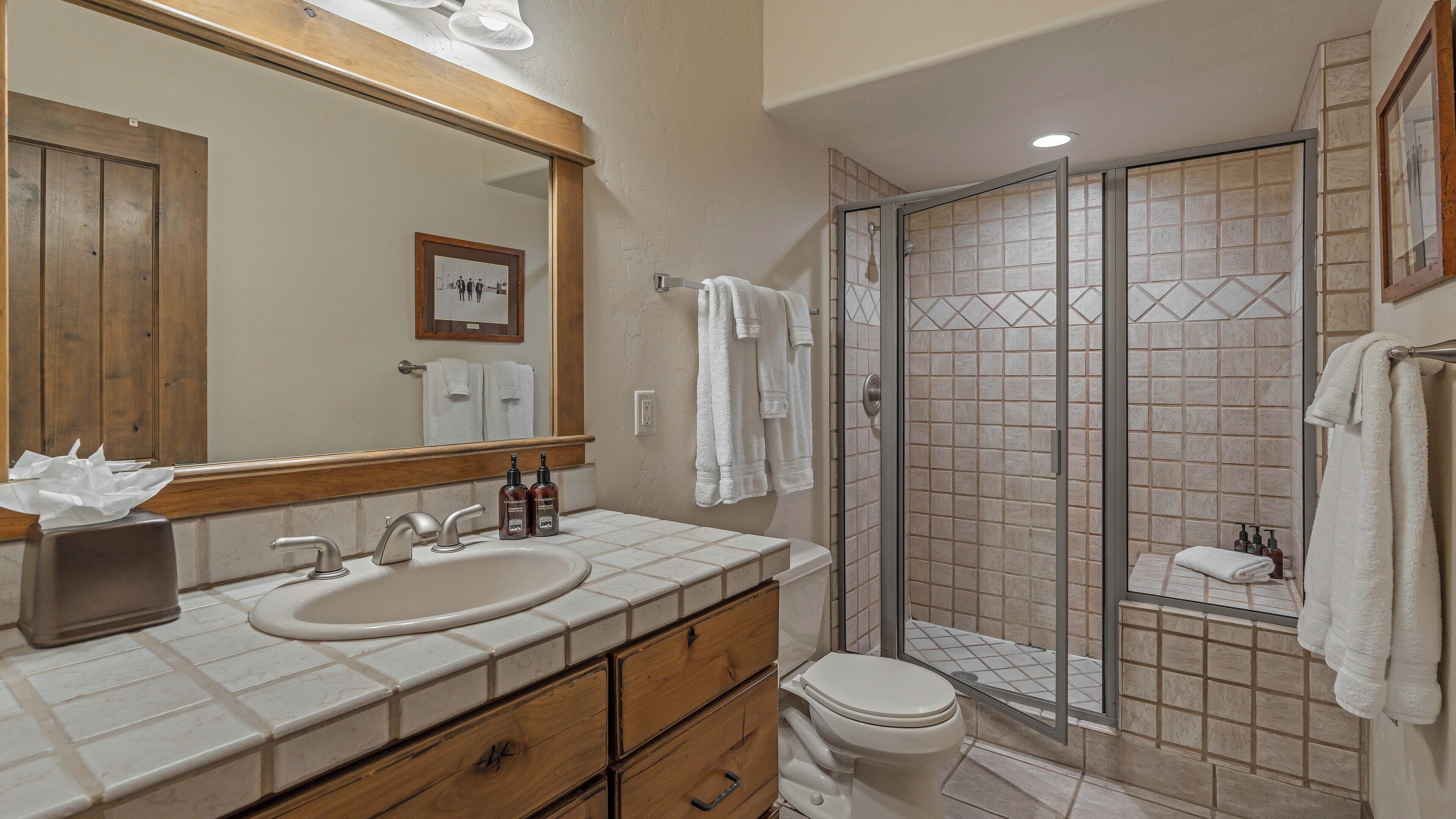 A bathroom with a sink, mirror, wooden vanity, and a glass-enclosed shower area.