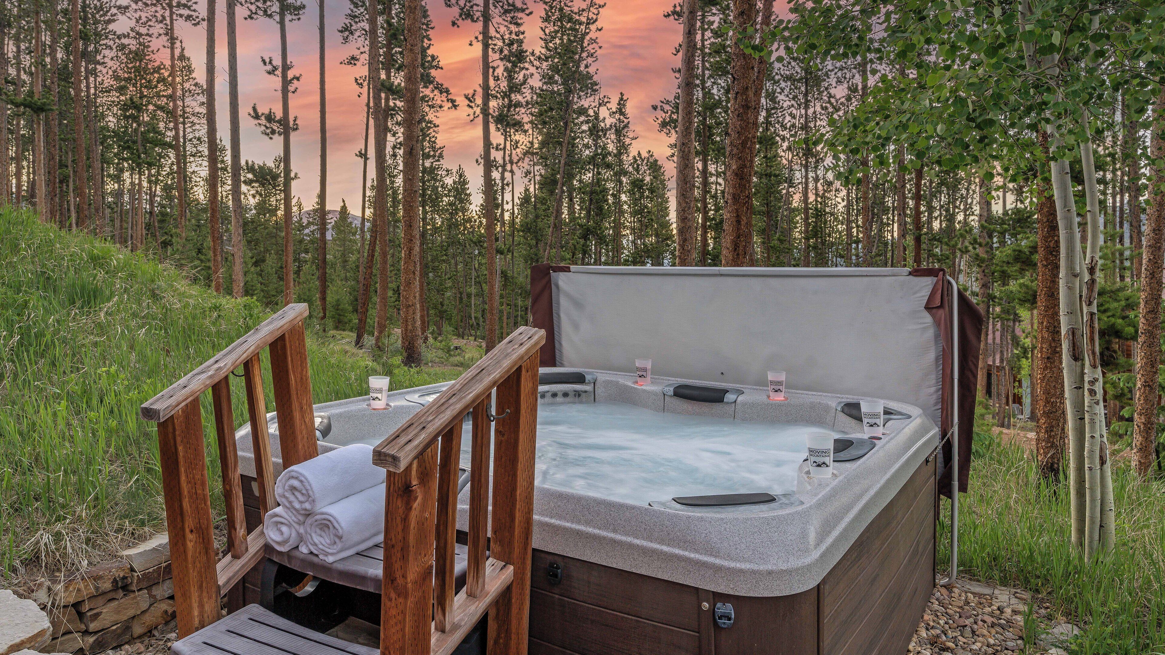 Un bain à remous doté de rampes en bois et agrémenté d’une serviette, le tout entouré d’une forêt.