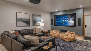 A modern living room with a black leather sofa, a coffee table with cookies, a chessboard, and a large flat-screen TV displaying a space scene.
