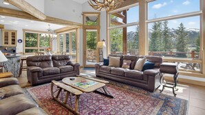 Ein geräumiges Wohnzimmer mit Ledersofas, einem Couchtisch und einem großen Fenster mit Blick auf die Berge.