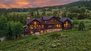 A large, multi-story log cabin with multiple windows and a balcony, surrounded by lush greenery and a forested hillside. - Hot Tub + Close to Skiing/Golf + Ski Shuttle - Monte Video (Breckenridge)