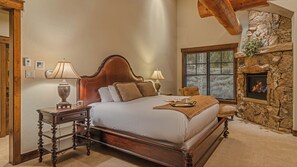 A bedroom with a large bed, two bedside tables with lamps, a stone fireplace, and a window with a view of trees. - Hot Tub + Close to Skiing/Golf + Ski Shuttle - Monte Video (Breckenridge)