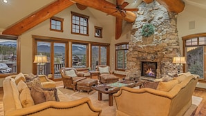 A spacious living room with a stone fireplace, leather furniture, and large windows offering mountain views.