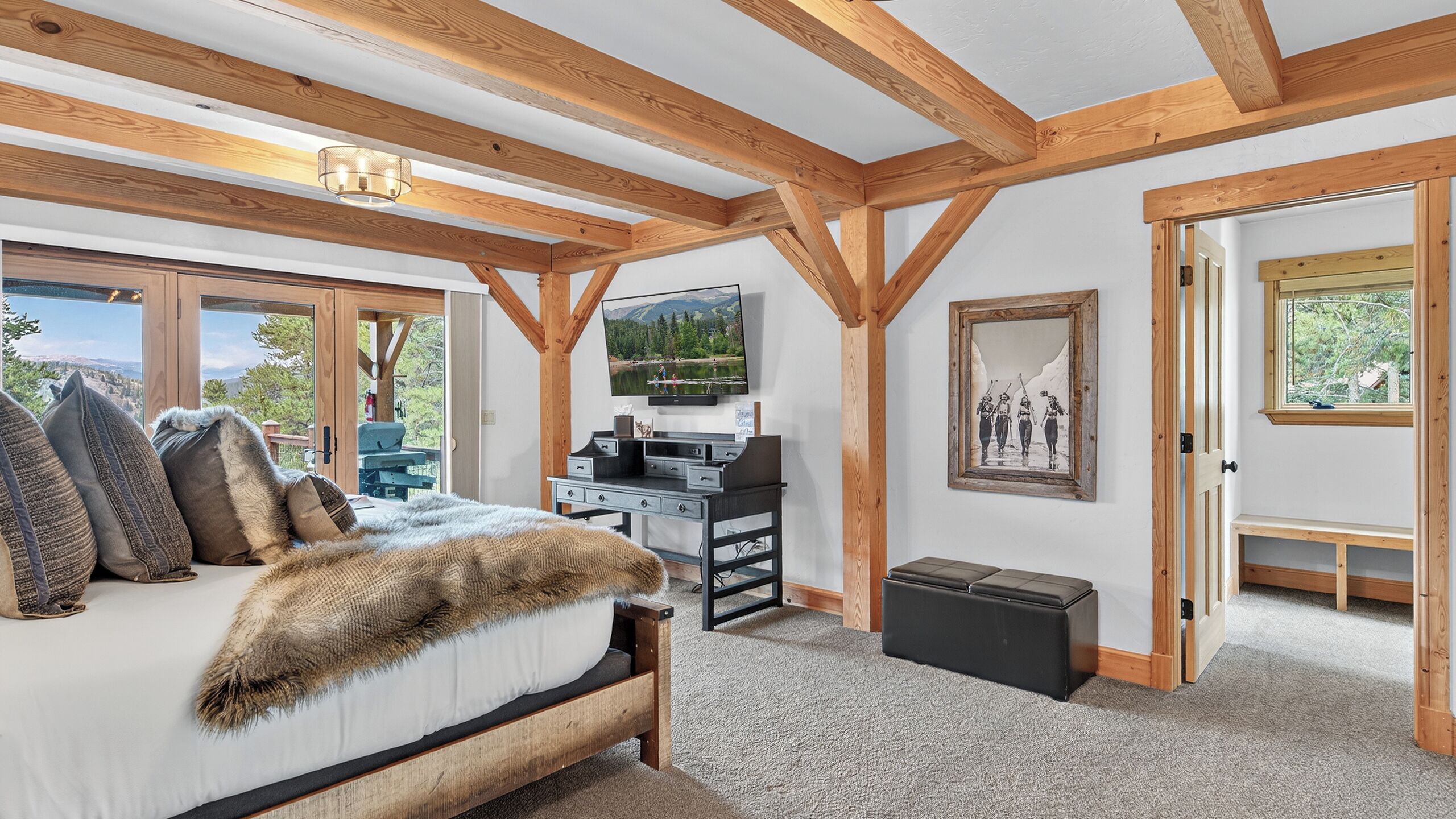 A bedroom with a bed, a desk, a television, and a painting.