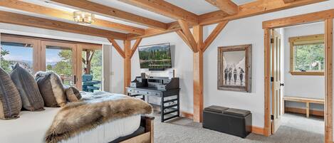 A bedroom with a bed, a desk, a television, and a painting.