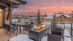 A patio with outdoor seating and a fire feature, overlooking a snow-covered landscape and buildings. - Hot Tub + Shuttle - On the Corner at The Shores (Breckenridge)