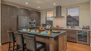 A modern kitchen with dark wood cabinets, stainless steel appliances, and a central island with seating. - Hot Tub + Shuttle - On the Corner at The Shores (Breckenridge)