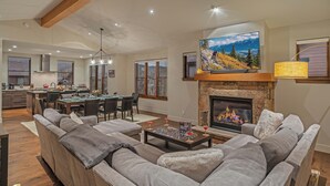 A spacious living room with a fireplace, a dining area, and a kitchen. - Hot Tub + Shuttle - On the Corner at The Shores (Breckenridge)