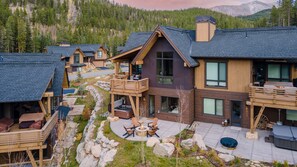 A modern lodge with a stone fireplace, outdoor seating, and a scenic mountain backdrop.