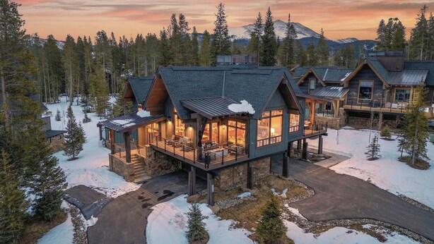 Un gran albergue de varios pisos con un porche cubierto y numerosas habitaciones, rodeado de nieve y árboles.