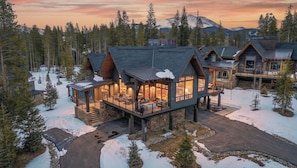 Un grand chalet à étages, doté d’une terrasse couverte et de nombreuses pièces, entouré de neige et d’arbres.