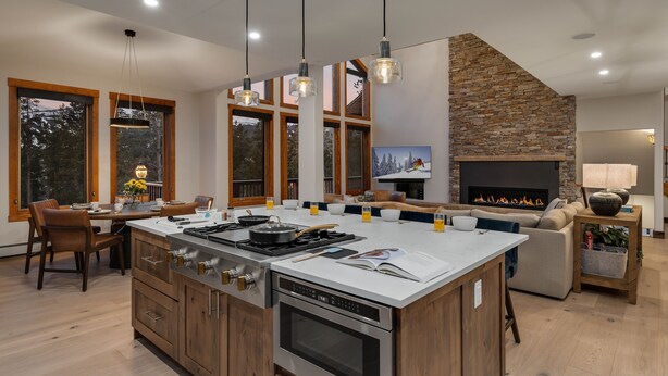 A modern kitchen with a large island, wooden cabinets, and a stone fireplace. - Spacious w/Mountain Views + Hot Tub + Close to Skiing - Mountain Gate (Breckenridge)
