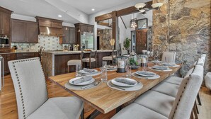 Une cuisine moderne avec des meubles de couleur bois foncé, un îlot central et un coin repas agrémenté d’une table en bois pouvant accueillir six personnes.