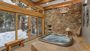 A spa area with a stone wall, a hot tub, wooden benches, and a view of a snowy landscape.