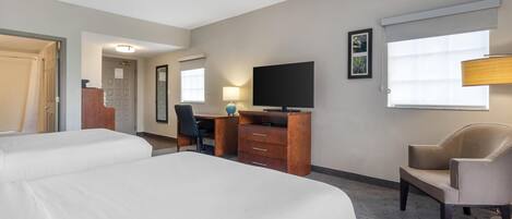 A hotel room with two beds, a desk, a television, and a chair.