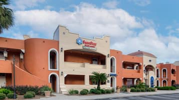 Un hotel con un letrero de 'SureStay Plus Hotel by Best Western', que cuenta con fachada de estuco, ventanas arqueadas y una palmera en primer plano.