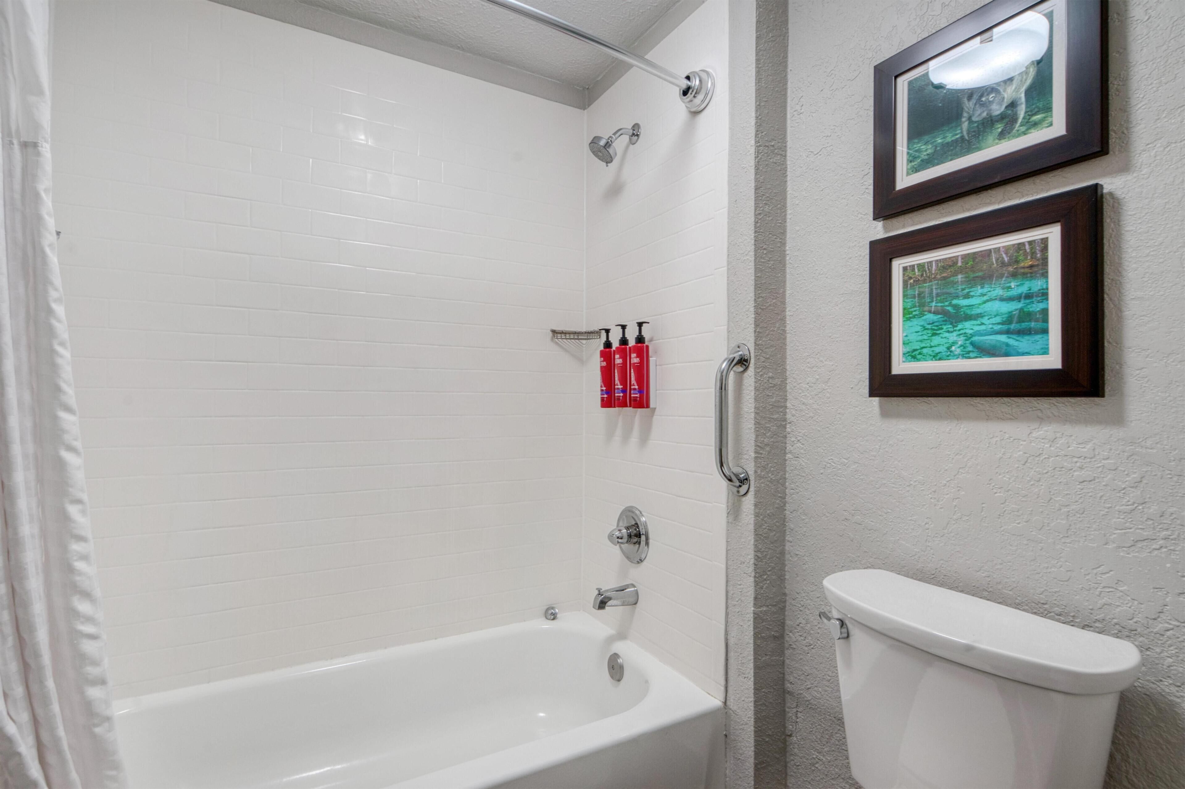A bathroom with a white bathtub, a toilet, and two framed pictures on the wall.