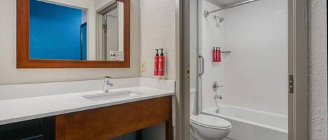 Une salle de bain avec un lavabo blanc, un miroir et des toilettes, un espace douche et un meuble-lavabo en bois avec des serviettes.