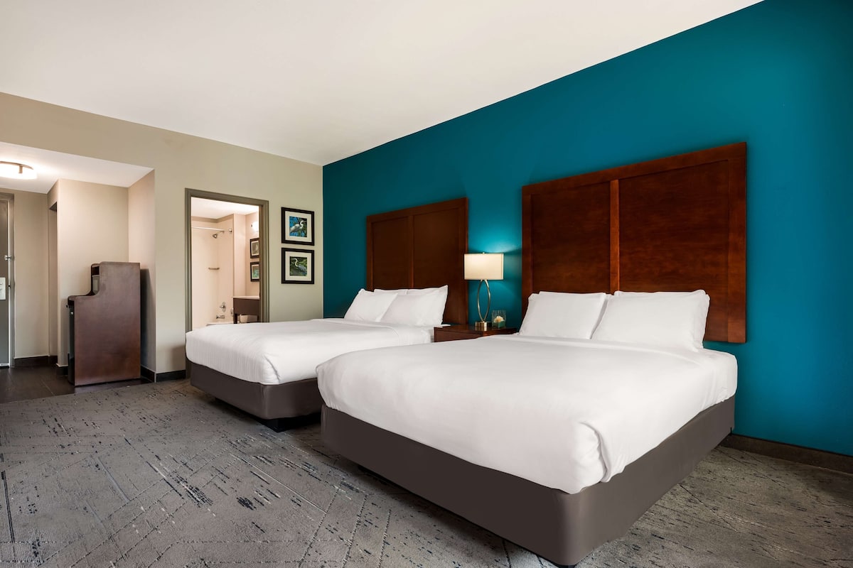 A hotel room with two beds, a wooden headboard, a desk, and a bathroom visible through an open door.