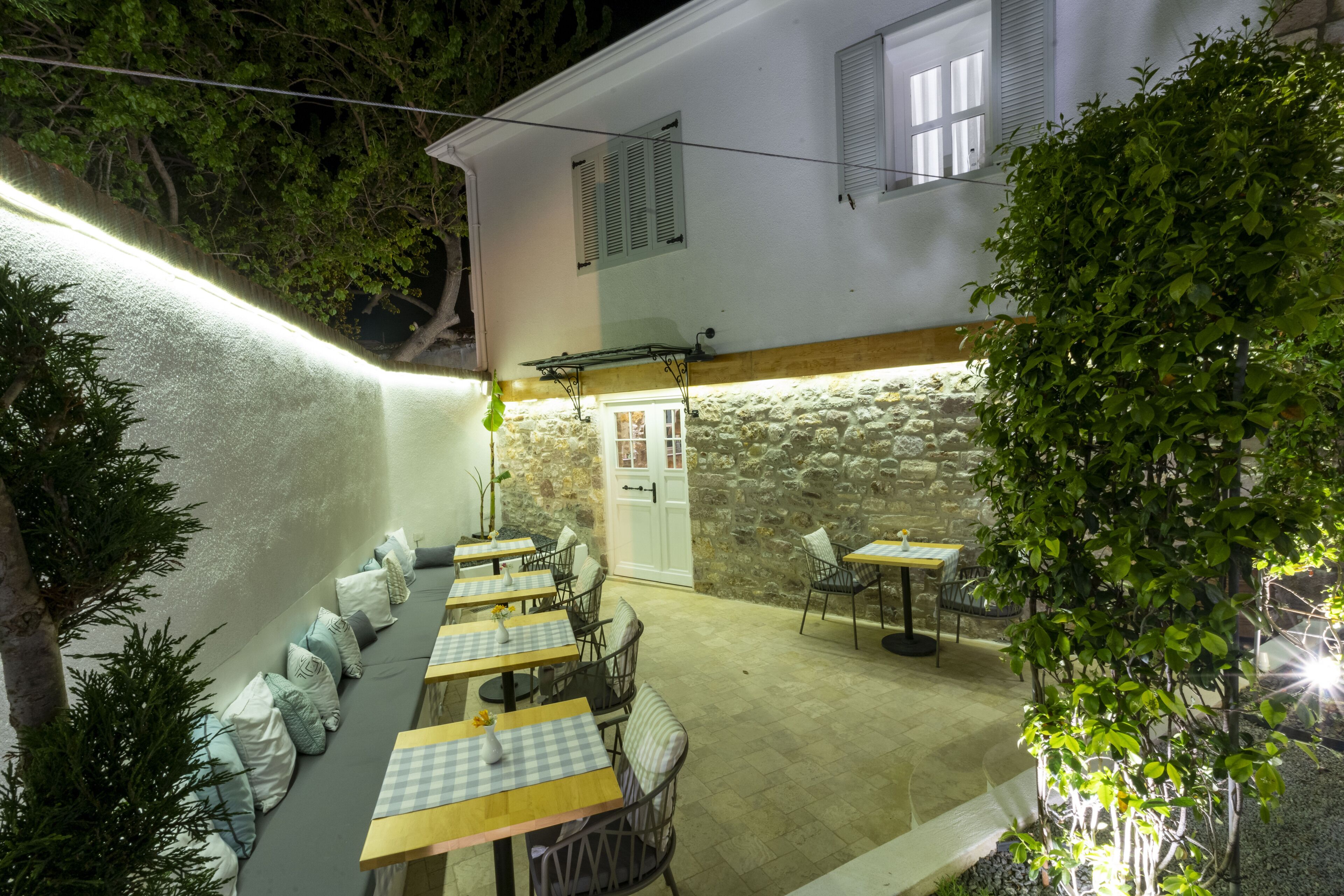 Un área de comedor al aire libre con mesas y sillas, un muro de piedra y una puerta.