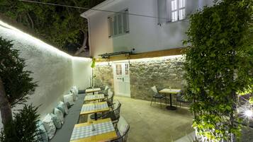 Un área de comedor al aire libre con mesas y sillas, un muro de piedra y una puerta.