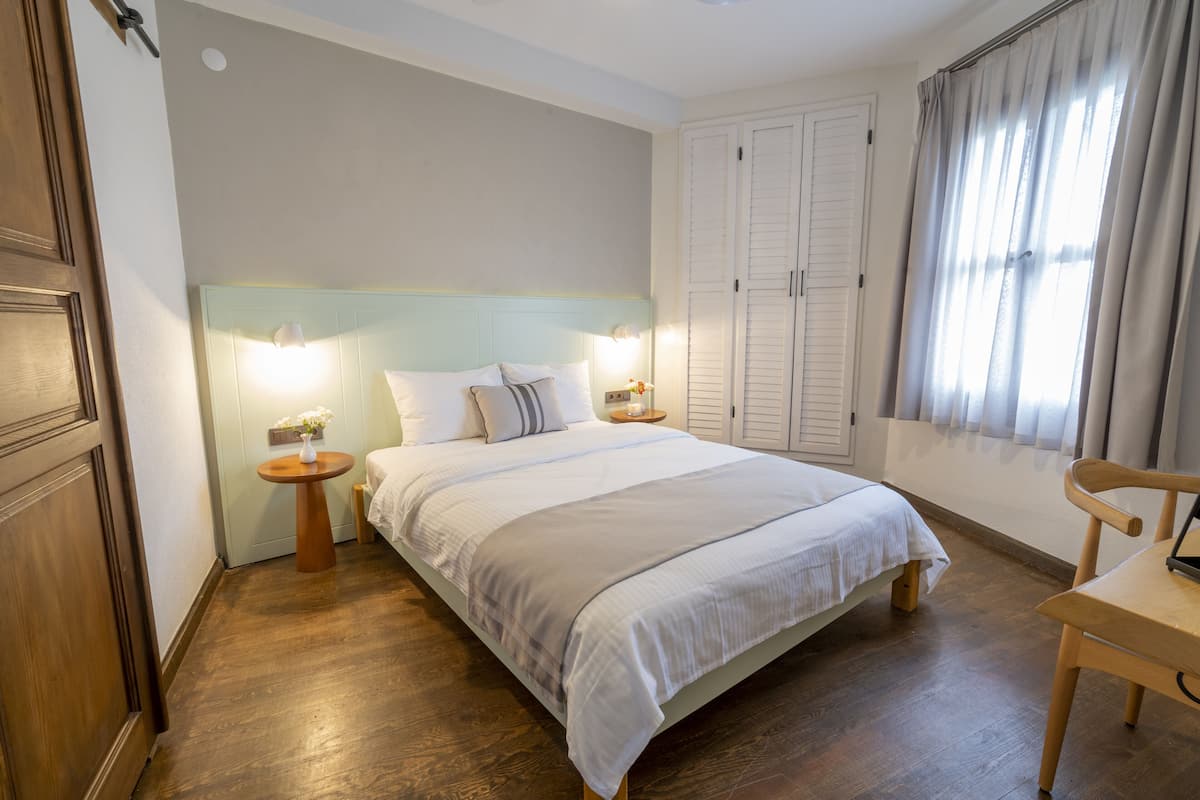 A bedroom with a bed, bedside tables, a chair, a wardrobe, and a window with curtains.