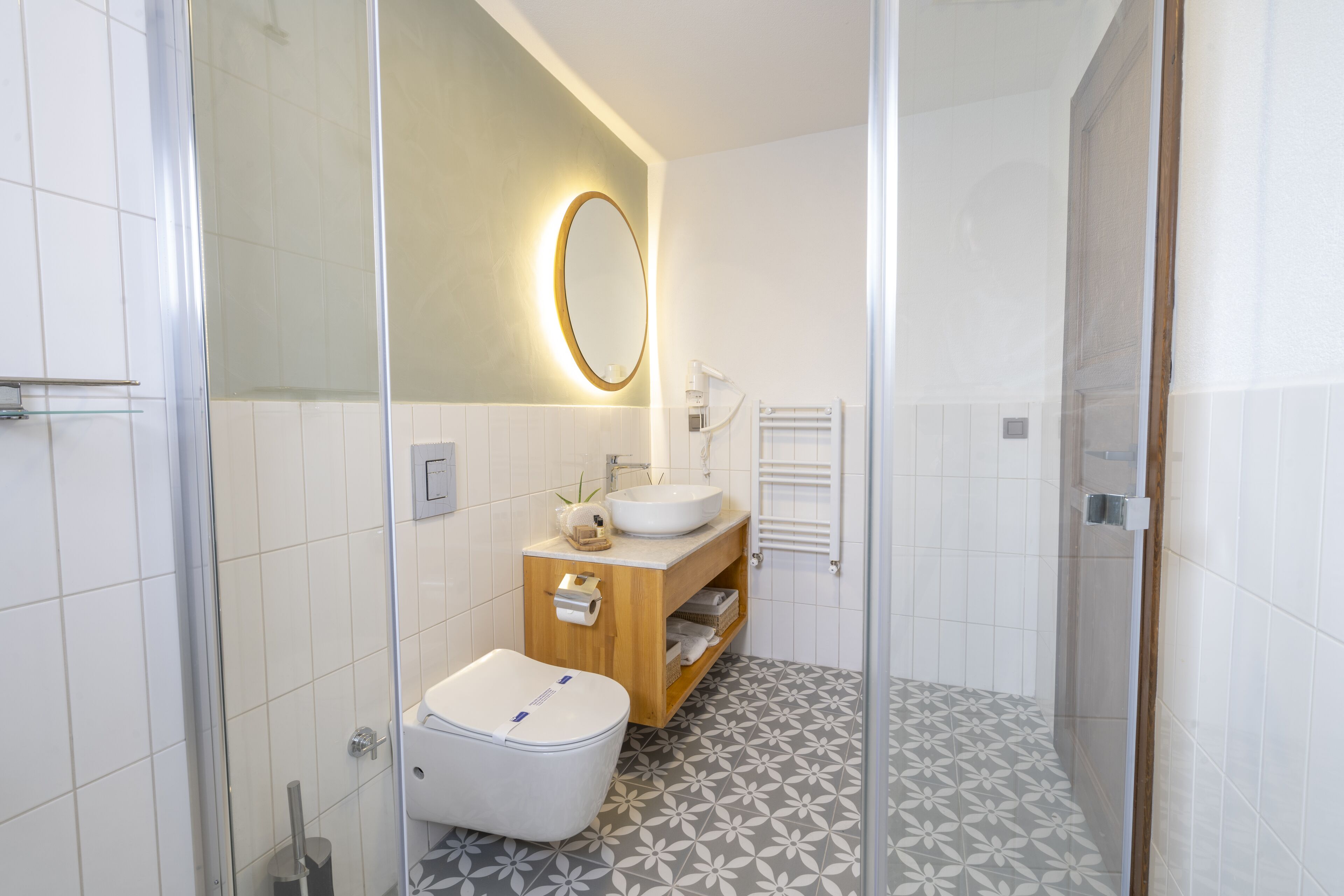 A modern bathroom with a glass shower enclosure, a wooden vanity with a sink, and patterned floor tiles.