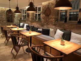 A cozy restaurant with wooden tables and chairs, a cushioned bench, and hanging pendant lights.