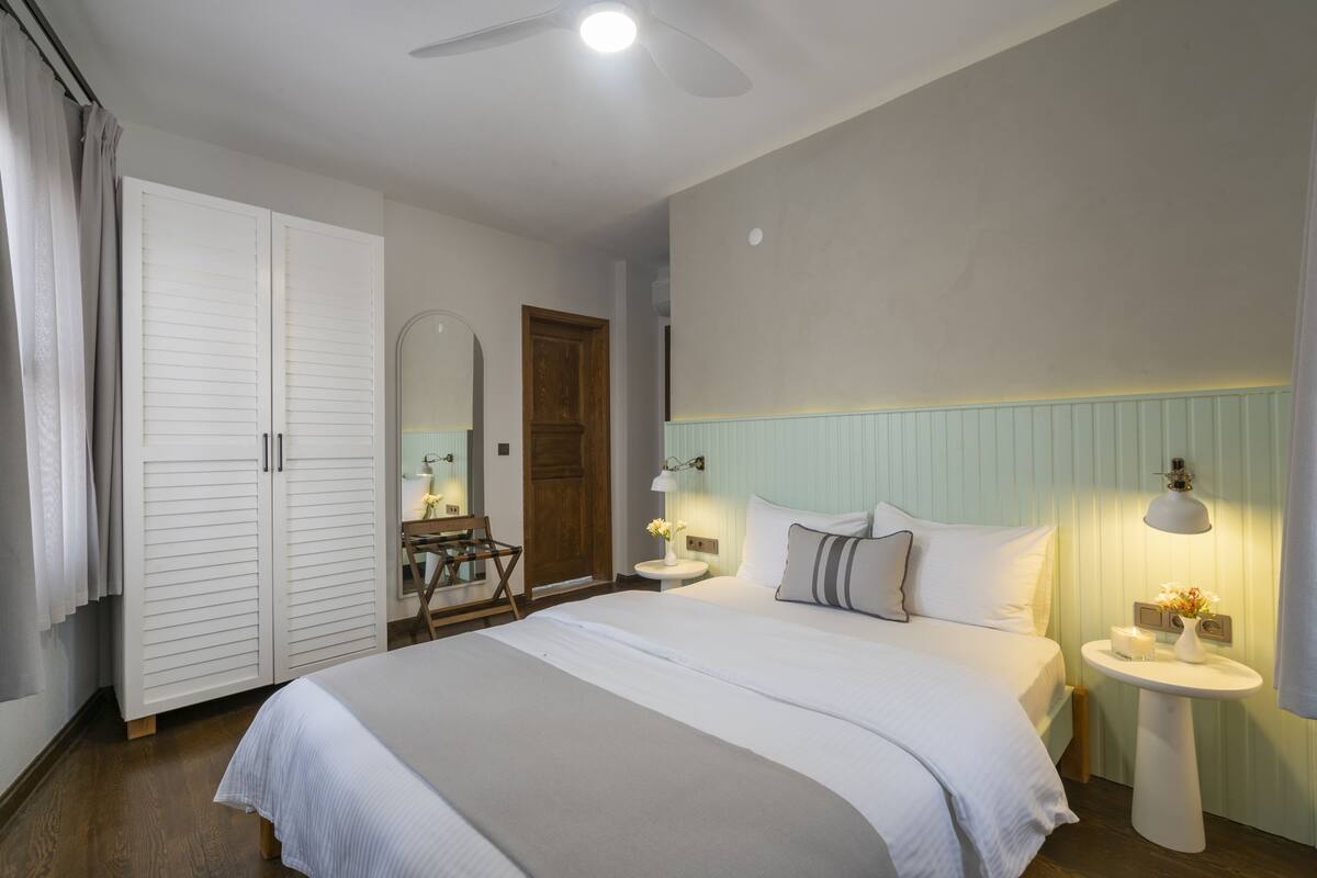 A bedroom with a bed, bedside tables, a wardrobe, a mirror, and a ceiling fan.