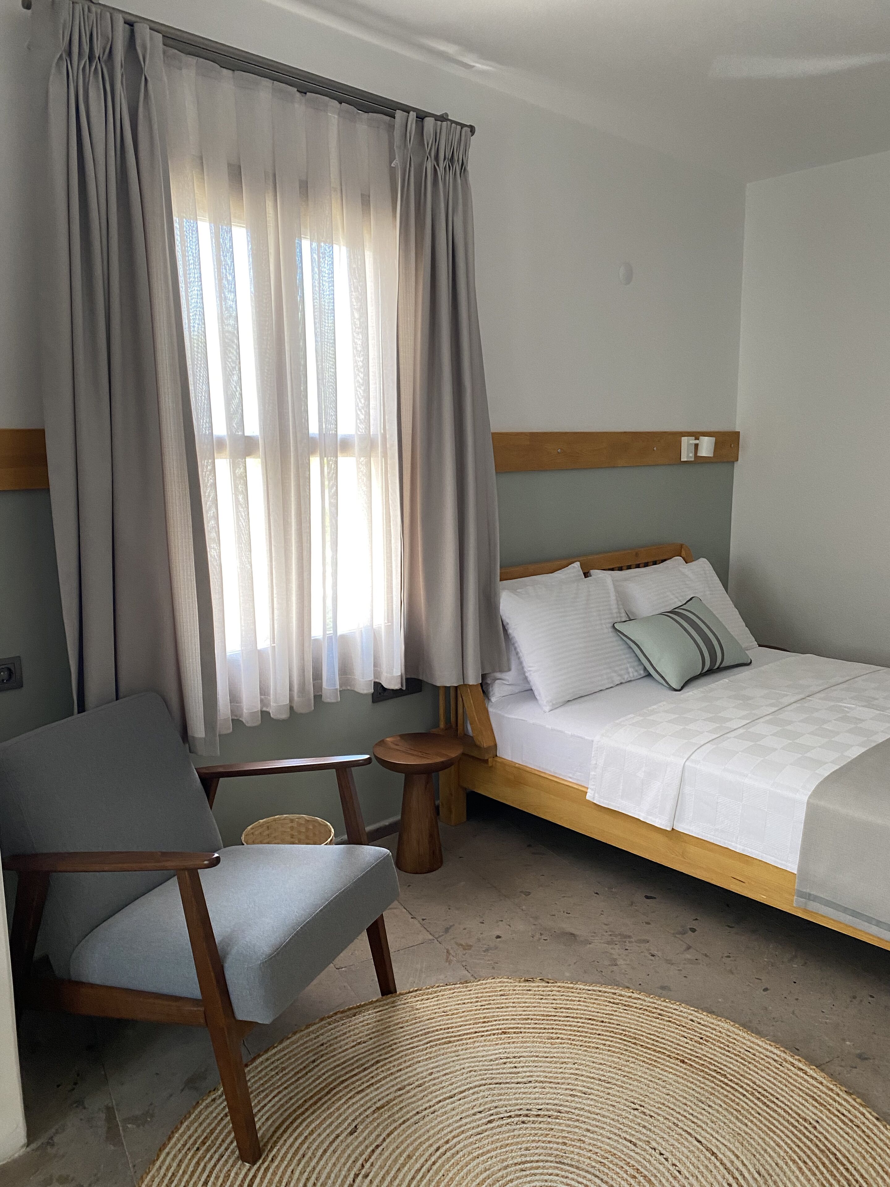 A bedroom with a bed, a chair, a small table, and a window with curtains.