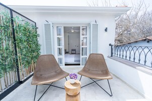 A balcony with two wicker chairs, a wooden table, and a potted plant.