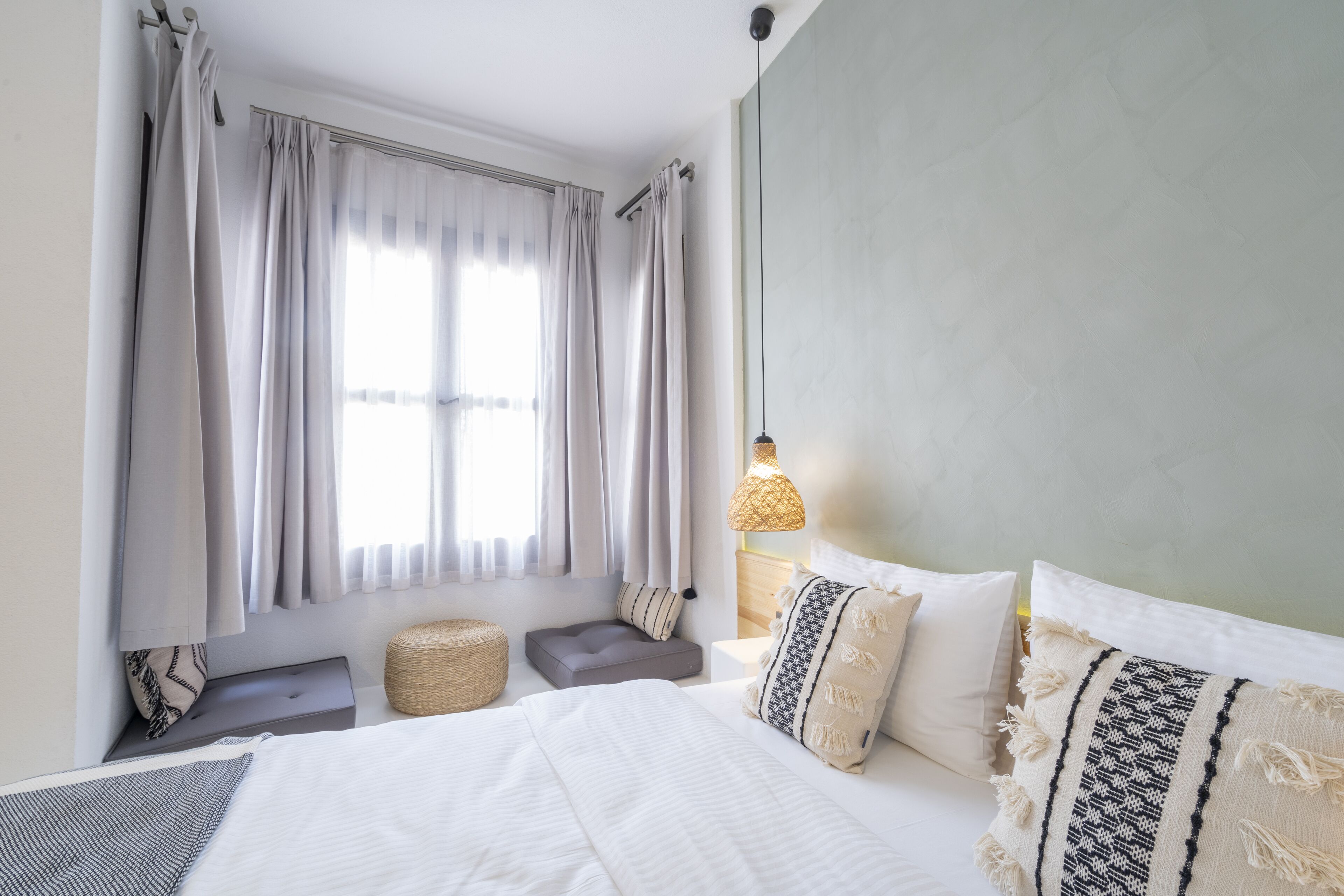 A bedroom with a bed, pillows, a bedside table, a lamp, and a window with curtains.