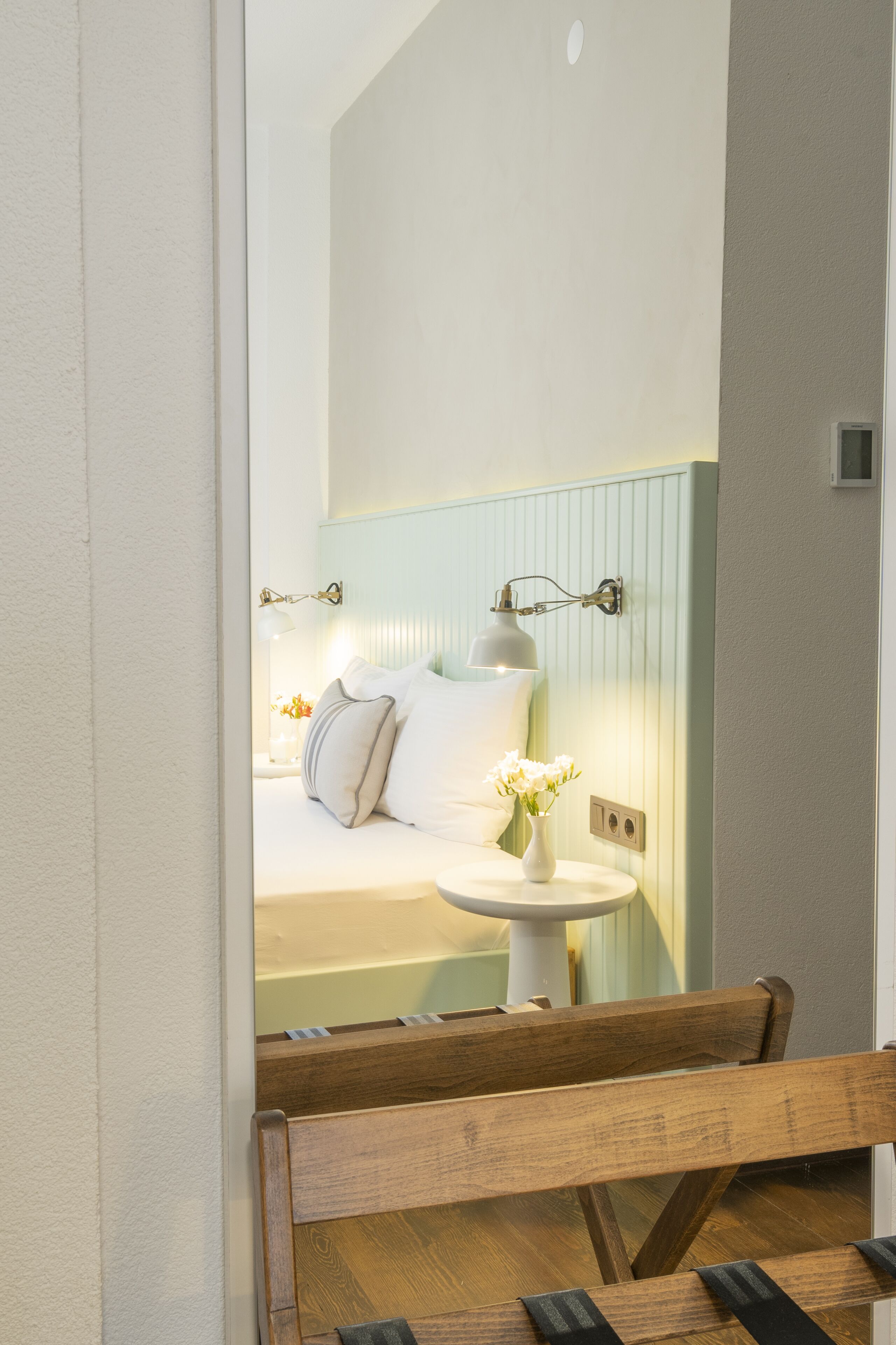 Un dormitorio con cama, mesita de noche, lámpara y un jarrón con flores.