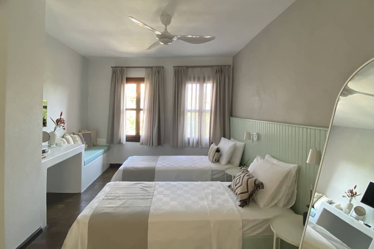 A hotel room with two beds, a ceiling fan, a desk, and a mirror.