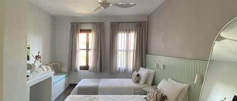 A hotel room with two beds, a ceiling fan, a desk, and a mirror.