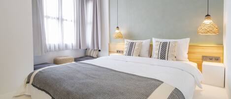 A modern bedroom with a large bed, two bedside lamps, a window with curtains, and a bedside table.