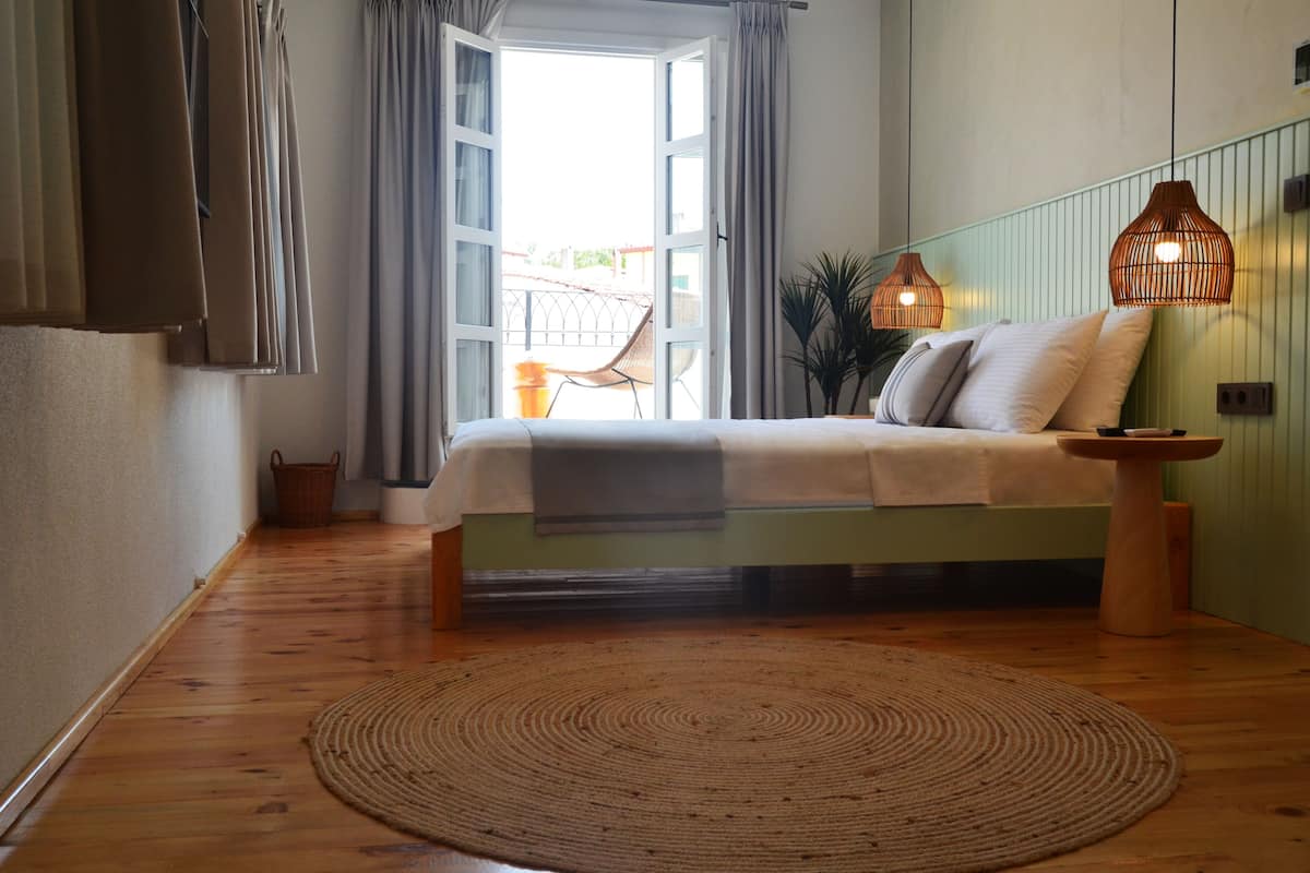A bedroom with a bed, a bedside table, a woven rug, and a window with curtains.