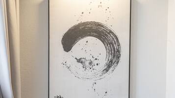 A framed abstract artwork on a wall, a wooden chair in front, and a curtain partially covering a window.