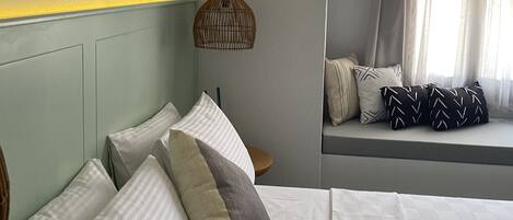 A bedroom with a bed, pillows, a bedside table, a hanging light fixture, and a window with curtains.