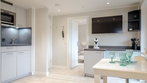 A modern kitchen with white cabinets, a built-in oven, and a coffee machine. There is a dining table with green glassware. - Ben, Tinnum, Germany (Sylt-Ost)