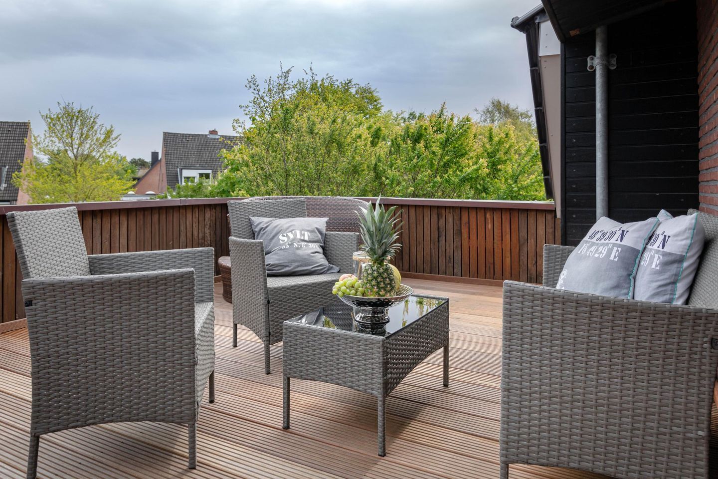 Une terrasse extérieure avec des meubles en osier, une table à plateau en verre et un centre de table décoré d’un ananas.