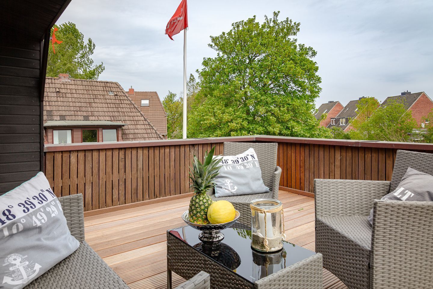 An outdoor seating area with wicker furniture, a table with a pineapple and a candle, and a flag.