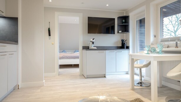 A modern kitchen with white cabinetry, a dining area with a white table and chairs, and a large window providing natural light. - Ben, Tinnum, Germany (Sylt-Ost)