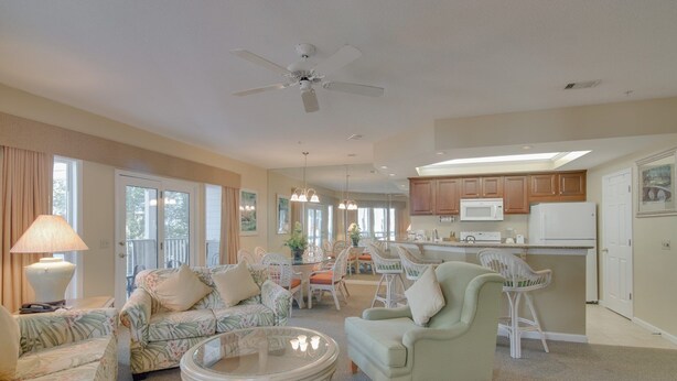A spacious living room with a sofa, armchair, and coffee table, a dining area with chairs, and a kitchen with cabinets and appliances.