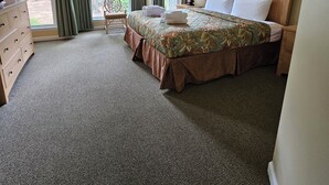 A hotel room with a bed, a chair, a dresser, and a ceiling fan.