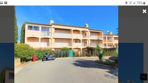 A multi-story building with balconies, a parking area, and a clear sky. - South-facing T2 apartment in village center with parking, swimming pool and tennis court. (La Croix Valmer)