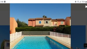 A swimming pool with a white fence, surrounded by a row of houses with red-tiled roofs and beige walls. - South-facing T2 apartment in village center with parking, swimming pool and tennis court. (La Croix Valmer)